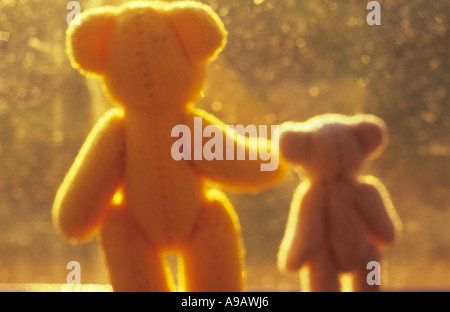 Impressionistic view from behind of mum or dad teddy bear with a young child ted standing at a window looking at golden sunlight Stock Photo