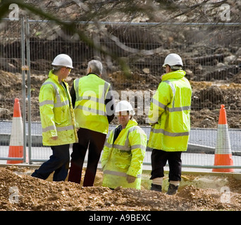 A group of builders wearing high vis reflective yellow coats and white hard hats. Site manager.  Road cones. Building site in UK Stock Photo