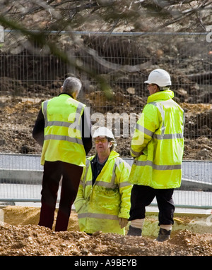 A group of workmen wearing yellow reflective coats and white hard hats. Site manager. Building site in the UK. Stock Photo