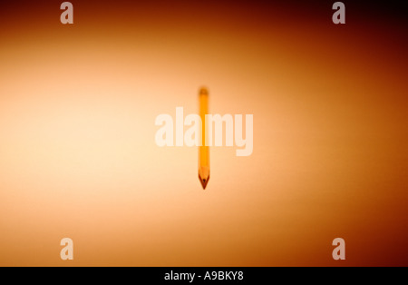 Pencil shown straight on lying on spotlit plain surface, sharpened tip in focus. Stock Photo