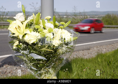 Car speeding past a floral tribute marking the spot of a fatal road traffic accident Stock Photo