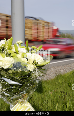 Death car and timber lorry speeding past a floral tribute marking the spot of a fatal road traffic accident Stock Photo