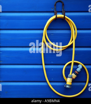 Curled yellow hosepipe hanging on blue wooden beach hut Stock Photo