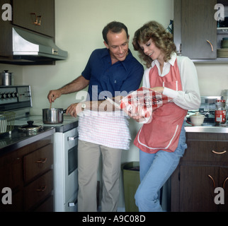 couple in kitchen cooking dinner with help of a recipe book Stock Photo