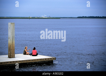 Two women chat while sitting on a pier in St Marys harbor Georgia after sunset Stock Photo