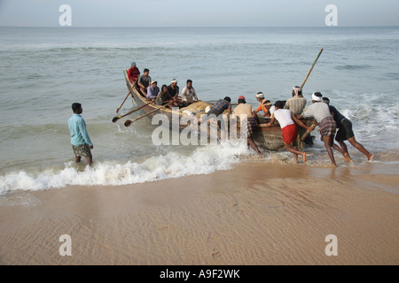 Fishermen push their traditional wooden boat from the beach into the sea in Varkala, Kerala, South India Stock Photo