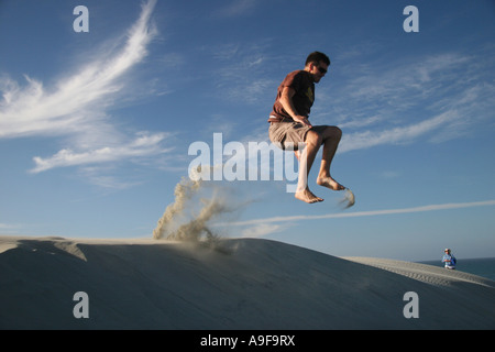 Tourist jumping off a huge crescent-shaped sand dune on a guided tour of Farewell Spit, Golden Bay, South Island, New Zealand Stock Photo