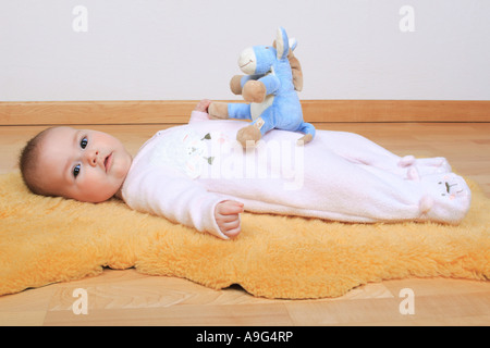 baby lying on a sheepskin rug, with a soft toy on his belly Stock Photo