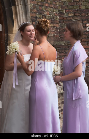 English bride having makeup adjusted while being attended to by her two bridesmaids before her wedding outside the church.  England, UK Stock Photo