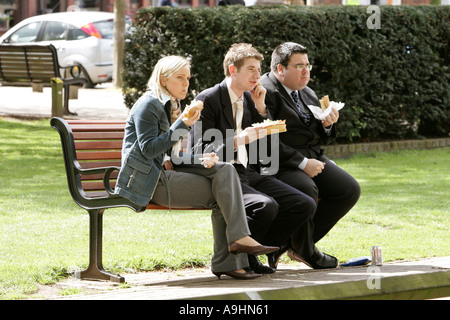 business trio enjoying lunch park bench noon break sharing discussing sandwich burger chips take way fast food hungry flirting l Stock Photo