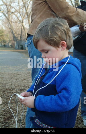 Three and one half (3 ½) year old American boy listens to music on his IPod music player in school yard. Stock Photo