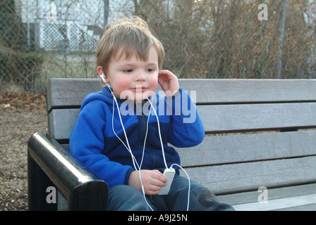 Three and one half (3 ½) year old American boy listens to music on his IPod music player in school yard. Stock Photo