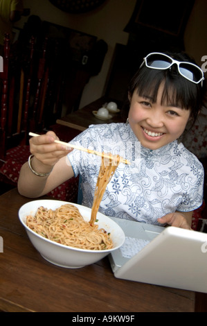 MODEL RELEASED YOUNG MIDDLE CLASS CHINESE WOMEN USING LAPTOP COMPUTER WHILE EATING NOODLES IN RESTAURANT BEIJING CHINA Stock Photo