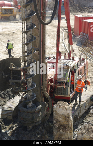 London close up pile boring auger attached to large piling rig beside exposed concrete pile with worker standing on caterpillar track England UK Stock Photo