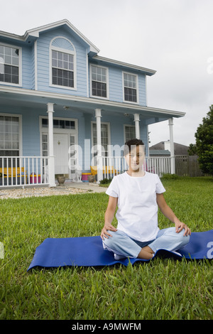 Pregnant woman sitting on exercise mat in front of house Stock Photo