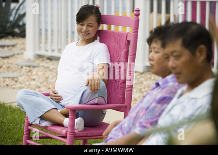 Pregnant woman sitting on rocking chair with her parents in foreground Stock Photo