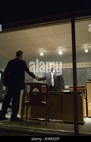 View through window of businessmen in office shaking hands Stock Photo