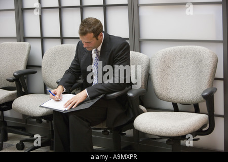 Businessman seated in an office writing in his folder Stock Photo