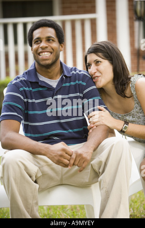 Smiling young inter-racial couple sitting on lawn chairs in front of house Stock Photo