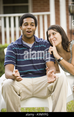 Smiling young inter-racial couple sitting on lawn chairs in front of house Stock Photo