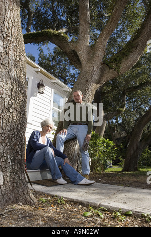 Mature couple on doorstep of home under large oak trees Stock Photo