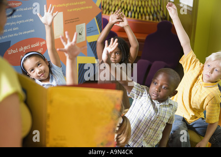 Students sitting in classroom, raising their hands to their teacher Stock Photo