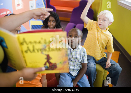 Students sitting in classroom, raising their hands to their teacher Stock Photo