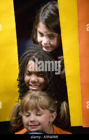 Three girls peeking out from behind a curtain Stock Photo
