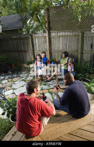 Two families sitting together on backyard patio, enjoying cold drinks Stock Photo