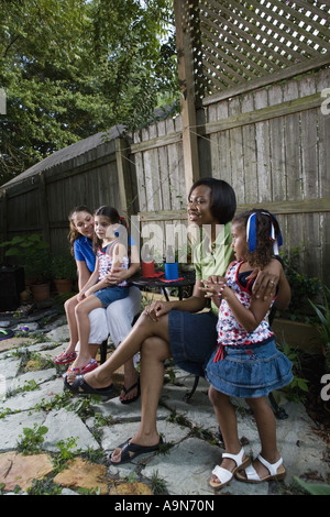 Two women sitting together on backyard patio with their young daughters Stock Photo