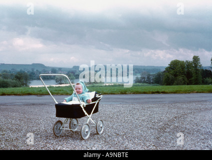 Caucasian baby sitting up in a pram with the British countryside in the distance. Circa 1960 Stock Photo