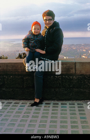 Young Caucasian woman and small child posing on the wall of Oliver's Mount with Scarborough and the North Sea in the distance circa1960. Stock Photo