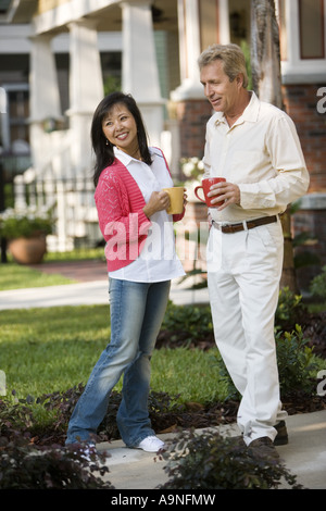 Affectionate mature inter-racial couple holding coffee mugs in front of their house Stock Photo