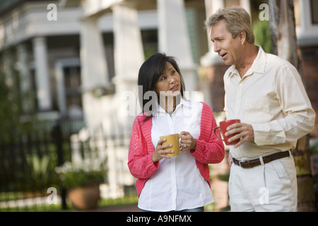 Affectionate mature inter-racial couple holding coffee mugs in front of their house Stock Photo