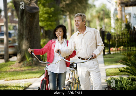 A mature inter-racial couple walking with bicycles in their neighborhood Stock Photo