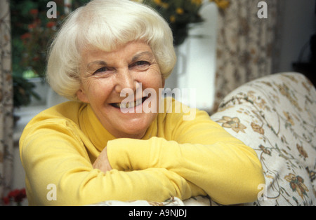 portrait happy grey haired mature woman leaning over back of sofa Stock Photo