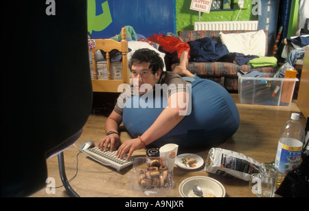 teenage boy computer nerd playing on computer in messy room surrounded by junk food Stock Photo