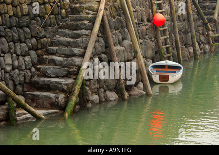 Small white dinghy and bright orange buoy secured to the historic 14th century stone built harbour wall at Clovelly North Devon Stock Photo