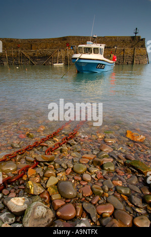 Small fishing boat moored to 2 heavy rusty metal chains in the historic 14th century stone built harbour at Clovelly Stock Photo