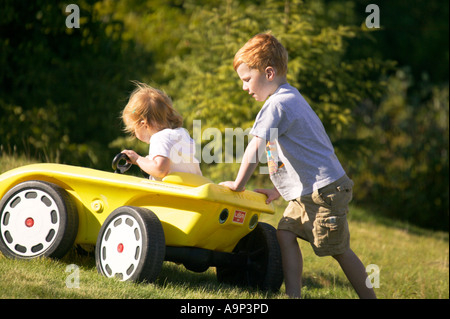 Brother pushing little sister in toy car Stock Photo