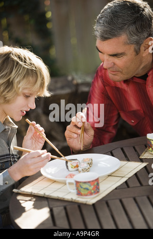 Father showing son how to eat sushi with chopsticks Stock Photo