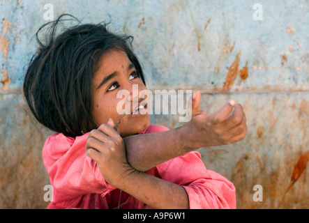 Indian child beggar holding out her hand sitting against a wall on the streets of Puttaparthi, Andhra Pradesh, India Stock Photo