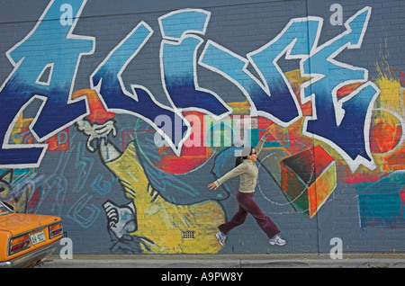 Young woman jumps in front of graffiti painted wall Stock Photo