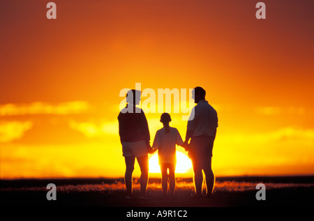 Family of three silhouetted by setting sun Stock Photo