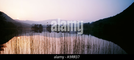 A golden sun sets over Rydal Water lake District Cumbria framed with mountains and reed beds Stock Photo