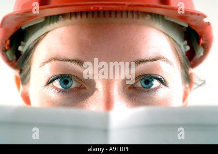 A young female architect wearing a red hard hat with architectural house plans Stock Photo