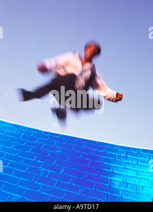 Businessman jumping over blue wall Stock Photo