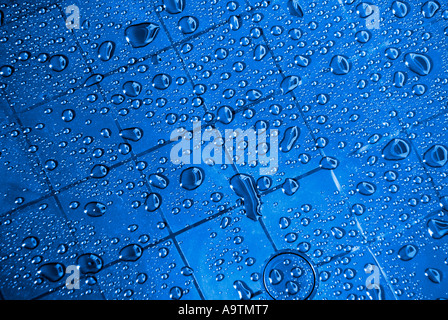Abstract arrangement of rainwater droplets on grid marks on new plastic garden table colour changed from green to blue via filter Essex England UK Stock Photo