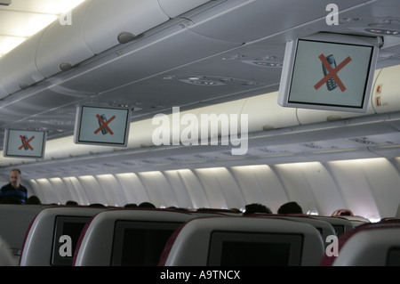 Monitor displaying no mobile phones symbol on a monitor hanging from the airplane cabin ceiling. Stock Photo