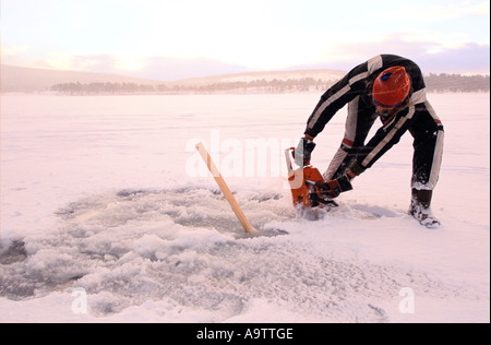 Hans Peter Strand uses a chain saw to cut a hole in the Torne river s ice sheet Stock Photo